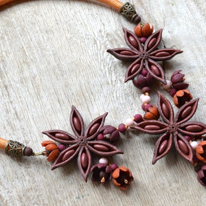 May include: A brown and orange necklace with star anise and flower charms. The necklace is made of a brown cord and has a metal clasp.