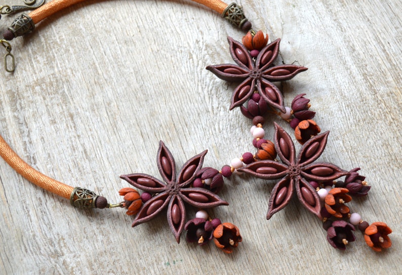 May include: A brown and orange necklace with star anise and flower charms. The necklace is made of a brown cord and has a metal clasp.