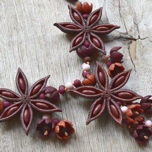 May include: A brown star anise necklace with burgundy and orange flower accents. The necklace is made of polymer clay and is strung on a brown cord.