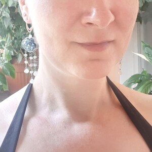 May include: A pair of silver dangle earrings with a blue and white cloud-shaped charm and white beads hanging from the bottom.