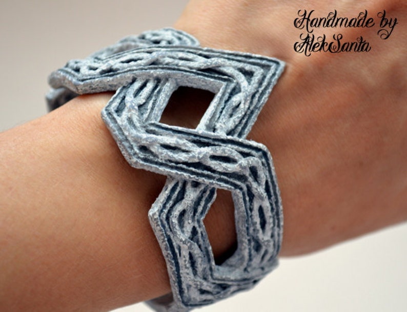 Puede incluir: Un brazalete de color plateado con un dise&ntilde;o geom&eacute;trico. El brazalete est&aacute; hecho de un material tejido y tiene una superficie texturizada. El brazalete est&aacute; hecho a mano por AlekSanta.