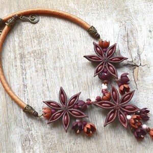 May include: A brown and orange necklace with star anise and flower-shaped beads. The necklace is made of cord and has a metal clasp.
