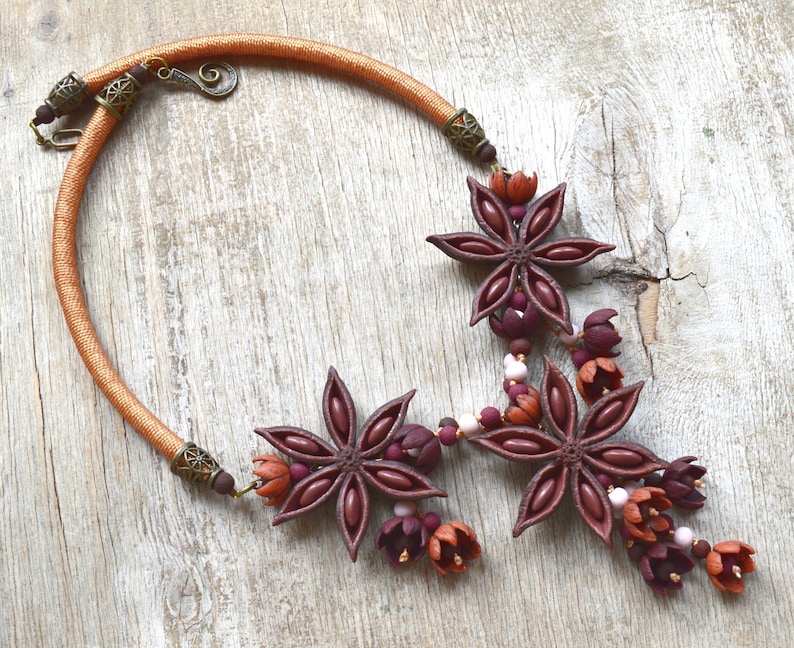 May include: A brown and orange necklace with star anise and flower-shaped beads. The necklace is made of cord and has a metal clasp.