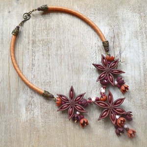 May include: A necklace made with a brown cord and star anise charms. The charms are decorated with small pink and red beads.