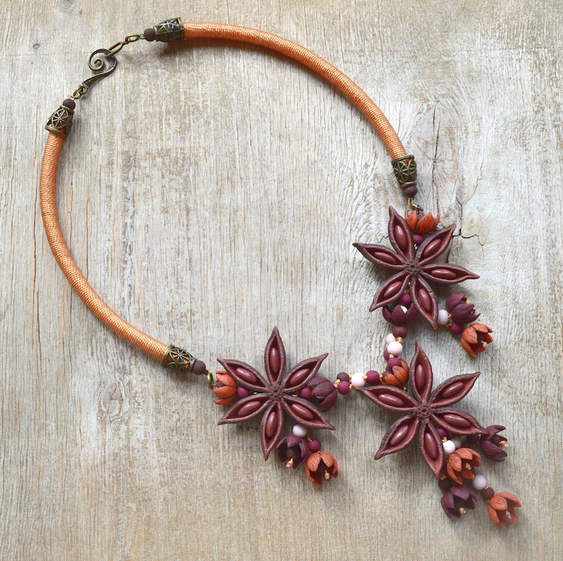 May include: A necklace made with a brown cord and star anise charms. The charms are decorated with small pink and red beads.