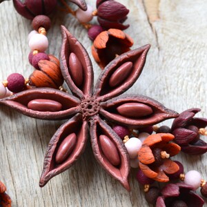 May include: A close-up of a brown star anise charm with visible seeds, part of a necklace made with polymer clay flowers in shades of burgundy, orange, and pink.