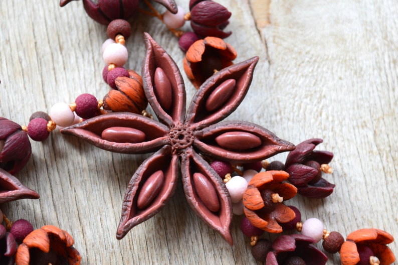 May include: A close-up of a brown star anise charm with visible seeds, part of a necklace made with polymer clay flowers in shades of burgundy, orange, and pink.