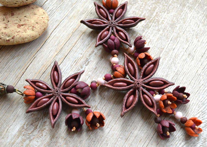 May include: A necklace made of brown star anise and burgundy, orange, and pink flower-shaped beads.