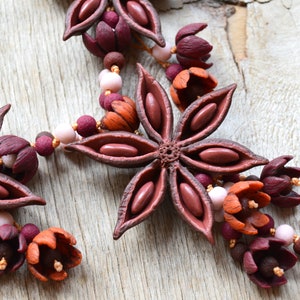 May include: A necklace made of brown star anise pods, burgundy and orange flowers, and pink and brown beads.