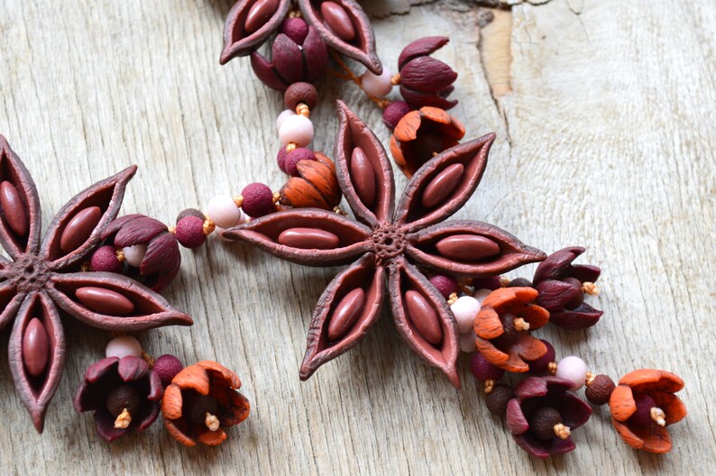 May include: A necklace made of brown star anise pods, burgundy and orange flowers, and pink and brown beads.
