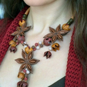 May include: A brown and red necklace made of star anise and other small floral shapes. The necklace is worn by a person with a red sweater.