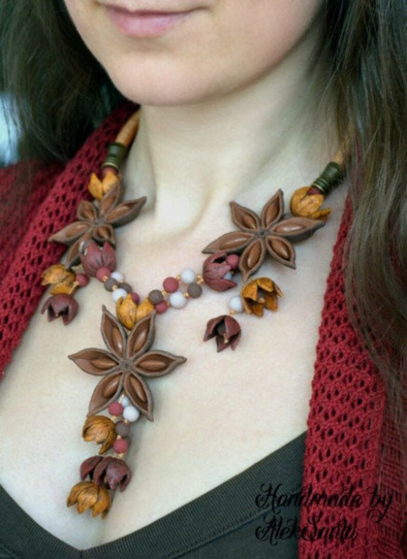 May include: A brown and red necklace made of star anise and other small floral shapes. The necklace is worn by a person with a red sweater.