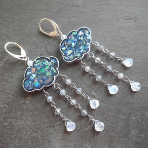 May include: A pair of silver earrings with a blue and green iridescent cloud charm and dangling moonstone beads.