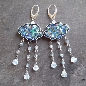 May include: A pair of silver earrings with a cloud-shaped design made of iridescent blue and green abalone shell. Each cloud has a dangling chain of silver beads and moonstone drops.