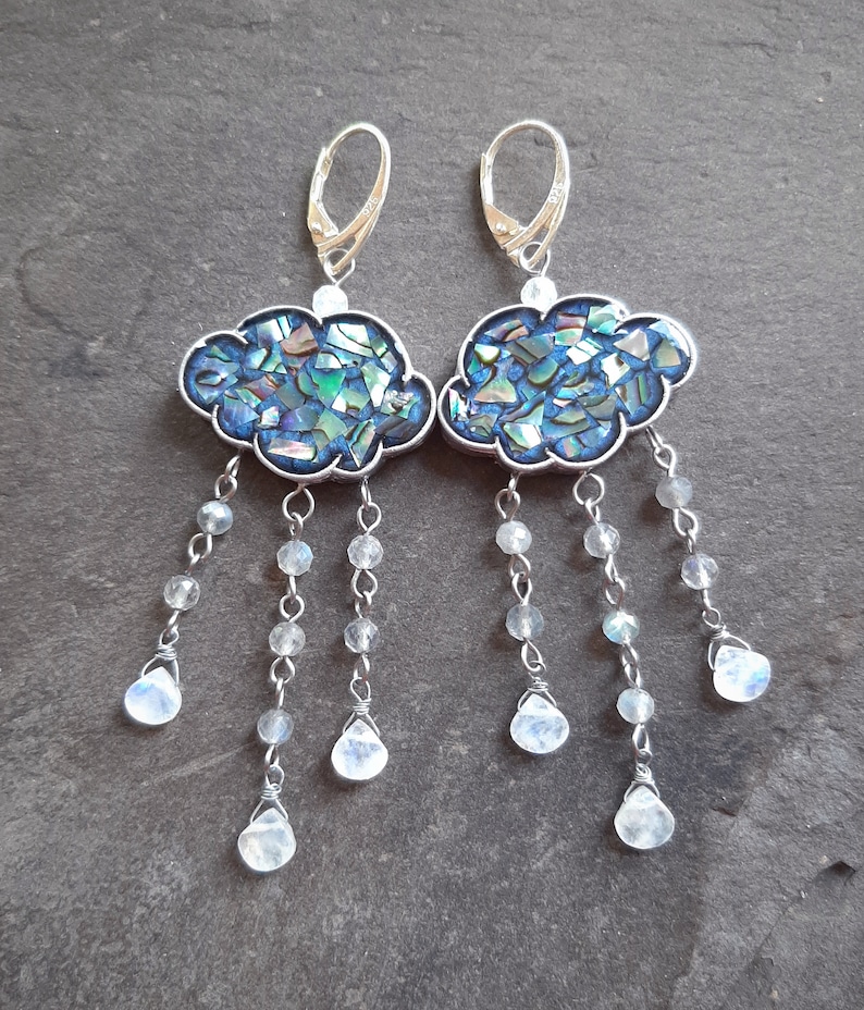 May include: A pair of silver earrings with a cloud-shaped design made of iridescent blue and green abalone shell. Each cloud has a dangling chain of silver beads and moonstone drops.