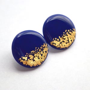 Peut inclure: Paire de boucles d'oreilles rondes bleues marine avec des accents de feuilles d'or. La feuille d'or est appliquée sur la moitié inférieure de chaque boucle d'oreille, créant un design unique et élégant. Accessoire de mode.