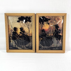 May include: Two framed vintage silhouette art pieces. Each features a black silhouette of figures in a park setting, set against a colorful background. The frames are a light gold color with ornate detailing.