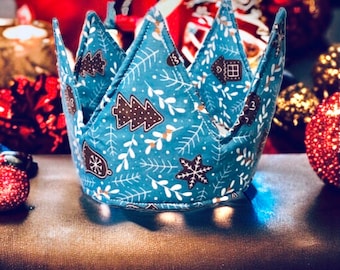 May include: A fabric crown with a festive Christmas pattern. The crown is teal with white sprigs and brown gingerbread shapes. The crown has six points and is designed for holiday celebrations.