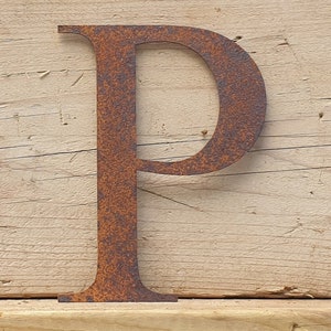 May include: A rusty metal letter P, with a rustic, aged look. The letter is standing upright on a wooden surface.