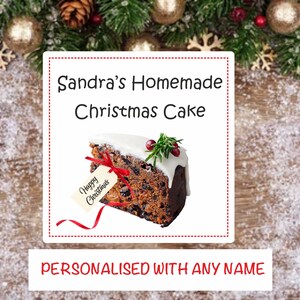 May include: A white label with red text that says "Sandra's Homemade Christmas Cake" and a picture of a slice of Christmas cake with white icing and a sprig of rosemary. The label also says "Personalised with any name".
