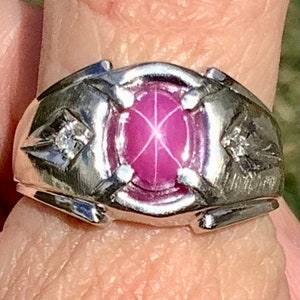 Op de afbeelding: Een zilveren ring met een roze edelsteen en twee kleinere diamanten. De ring heeft een gedetailleerd ontwerp met een verhoogde rand rond de edelsteen.