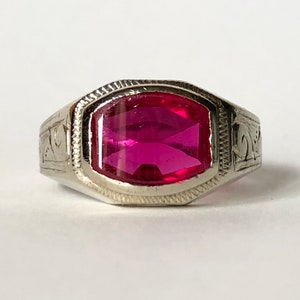 May include: A silver ring with an ornate design and a large, faceted, pink gemstone.