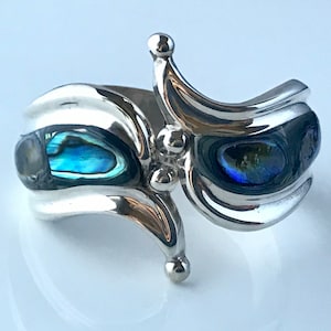 May include: A silver bracelet with a unique design featuring two abalone shell insets. The bracelet has a curved shape and a decorative detail on the top.