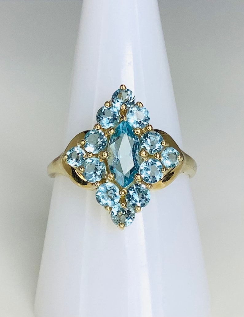 May include: A gold ring with a large marquise-shaped blue topaz gemstone surrounded by smaller round blue topaz gemstones.