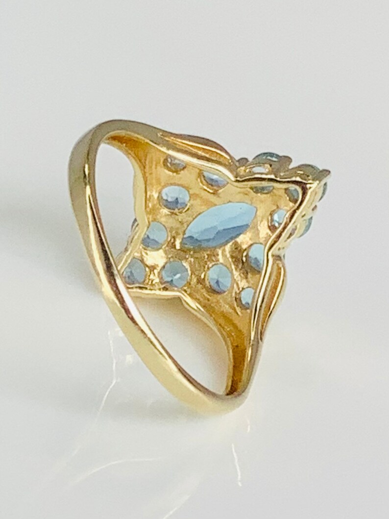 May include: A gold ring with a large blue gemstone surrounded by smaller blue gemstones.