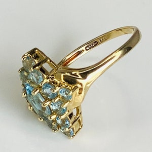May include: A gold ring with a cluster of light blue gemstones set in a heart shape. The ring is marked "CMO 14K" on the inside band.
