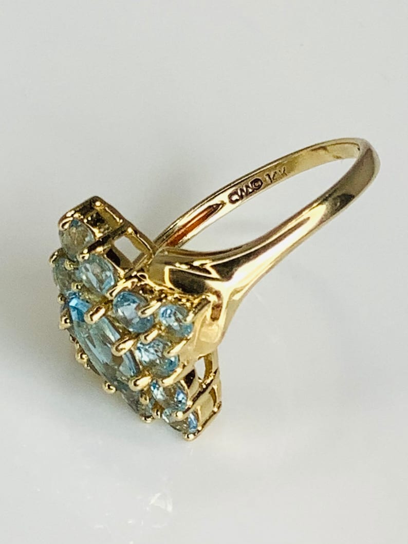 May include: A gold ring with a cluster of light blue gemstones set in a heart shape. The ring is marked "CMO 14K" on the inside band.