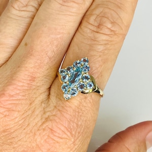 May include: A gold ring with a large blue topaz center stone surrounded by smaller blue topaz stones.