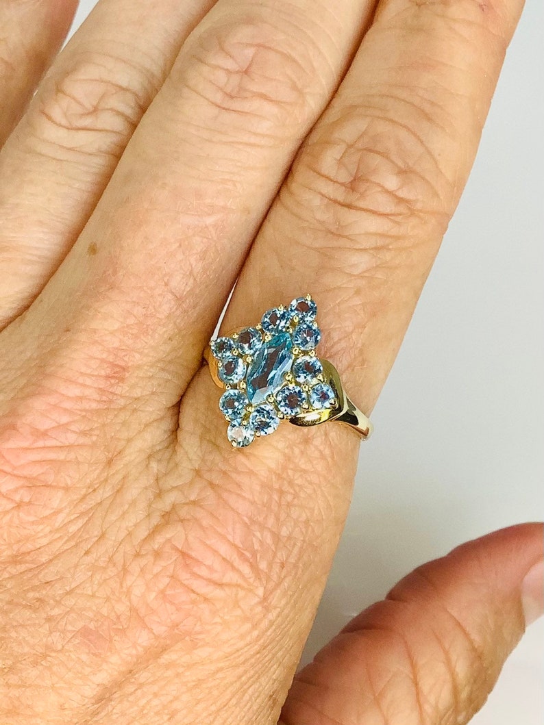 May include: A gold ring with a large blue topaz center stone surrounded by smaller blue topaz stones.