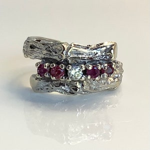 May include: A silver ring with a textured, branch-like design. The ring is set with five red rubies and one clear diamond.