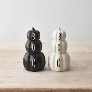 May include: Two ceramic pumpkin decorations, one black and one white, each with the word "BOO" in white lettering. The pumpkins are stacked and have a glossy finish. Ideal for Halloween.
