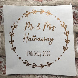 May include: Gold vinyl sticker with a wreath of leaves and the text "Mr & Mrs Hathaway" and "17th May 2022".