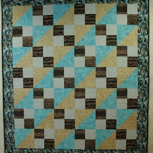 May include: A quilt with a geometric pattern of brown, white, and blue squares and triangles. The quilt is framed with a green and brown border.
