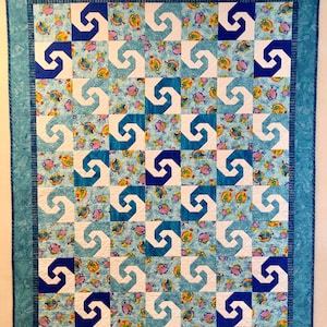 May include: A quilted wall hanging with a repeating pattern of white and blue swirls on a light blue background. The background fabric features colorful fish. The quilt has a turquoise border.