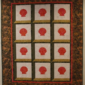 May include: A quilt with a repeating pattern of red seashells in a grid pattern. The quilt is framed with a brown and orange border.