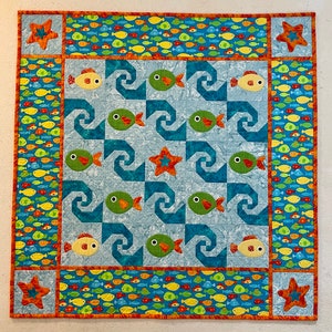 May include: A blue and white quilt with a pattern of fish and seashells. The quilt is bordered with a band of orange and yellow fabric with a pattern of fish.