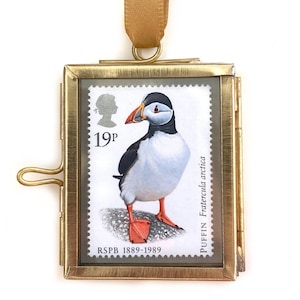 May include: A gold-toned metal frame with a glass front holds a 19p British postage stamp featuring a puffin. The stamp is from 1989 and reads "RSPB 1889-1989" and "PUFFIN Fratercula arctica".