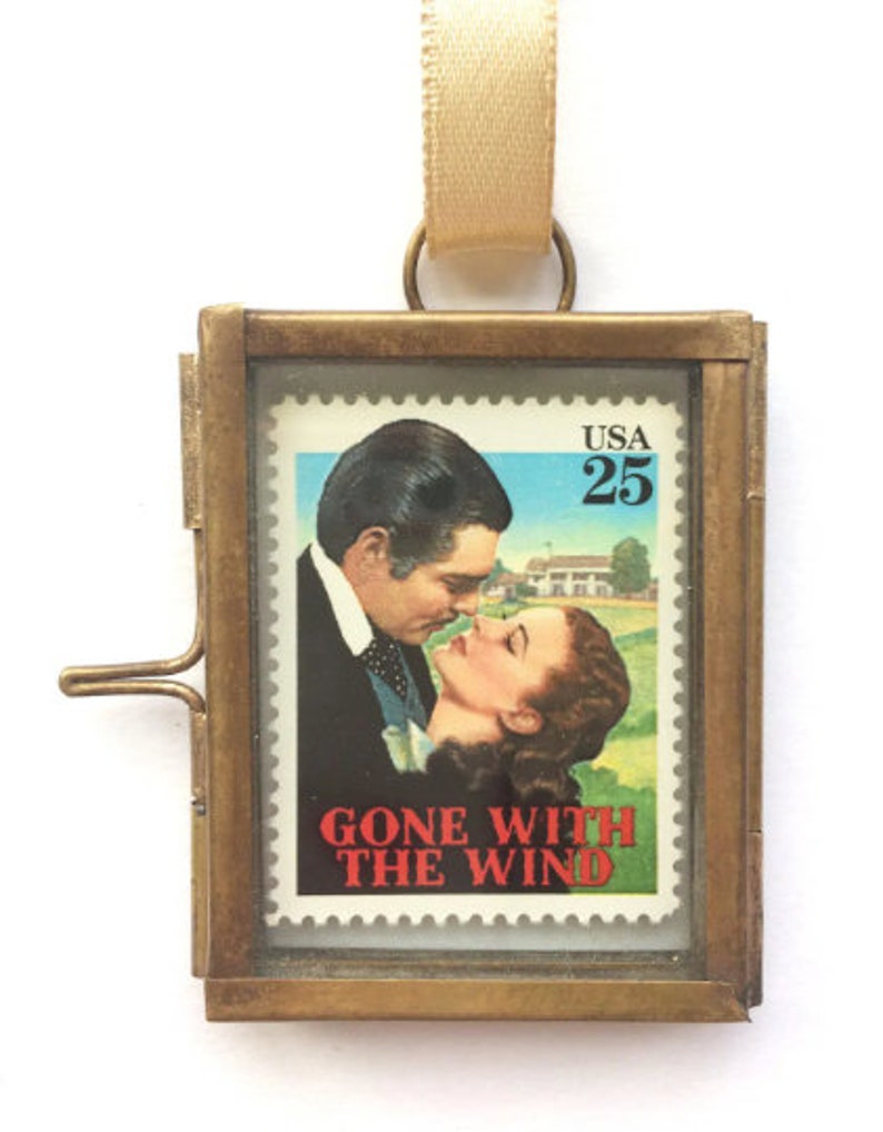 K&ouml;nnte beinhalten: Ein Messingrahmen-Medaillon mit einer Glasfront, das einen Vintage-Briefmarken "Vom Winde verweht" zeigt. Die Briefmarke zeigt eine Szene aus dem Film mit Clark Gable und Vivien Leigh. Die Briefmarke stammt aus den Vereinigten Staaten und hat einen Wert von 25 Cent.