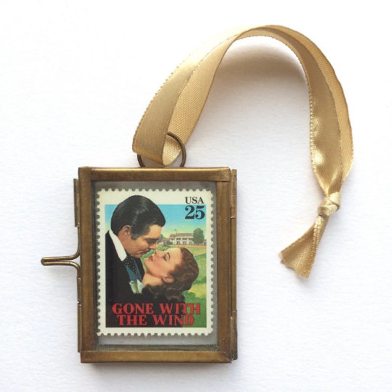 K&ouml;nnte beinhalten: Ein Messing-Bilderrahmen-Anh&auml;nger mit einer Vintage-Briefmarke "Vom Winde verweht" mit einem Schwarzwei&szlig;bild von Clark Gable und Vivien Leigh. Die Briefmarke ist in einem klaren Glas gerahmt und hat ein goldenes Band.