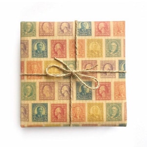 Op de afbeelding: Een bruine papieren cadeauzak met een patroon van vintage postzegels met portretten van historische figuren. De zak is vastgebonden met touw en een strik.