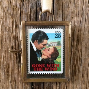 K&ouml;nnte beinhalten: Ein Ornament mit Messingrahmen, das eine alte US-Briefmarke "Gone With The Wind" mit einem Portr&auml;t von Clark Gable und Vivien Leigh zeigt. Die Briefmarke ist in klarem Glas gerahmt und hat einen Messingaufh&auml;nger.