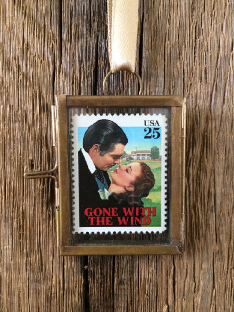 K&ouml;nnte beinhalten: Ein Ornament mit Messingrahmen, das eine alte US-Briefmarke "Gone With The Wind" mit einem Portr&auml;t von Clark Gable und Vivien Leigh zeigt. Die Briefmarke ist in klarem Glas gerahmt und hat einen Messingaufh&auml;nger.