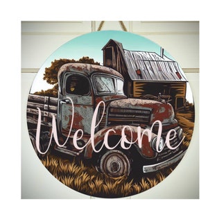 May include: A round welcome sign featuring a rusty red truck parked in front of a barn. The truck is situated in a field of tall grass. The word "Welcome" is written in pink cursive lettering.