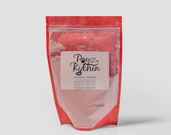Può includere: Un sacchetto rosso richiudibile pieno di polvere minerale rosa. Un'etichetta bianca mostra il testo "Pawz Kitchen" in un carattere corsivo, insieme a "Mineral Powder" e altro testo. Il sacchetto è sigillato e si erge su uno sfondo bianco.