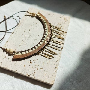 May include: A wooden and brass necklace with a geometric design and a fringe of brass accents.