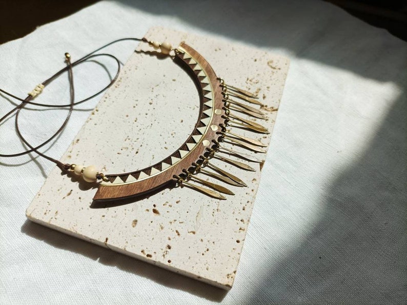 May include: A wooden and brass necklace with a geometric design and a fringe of brass accents.